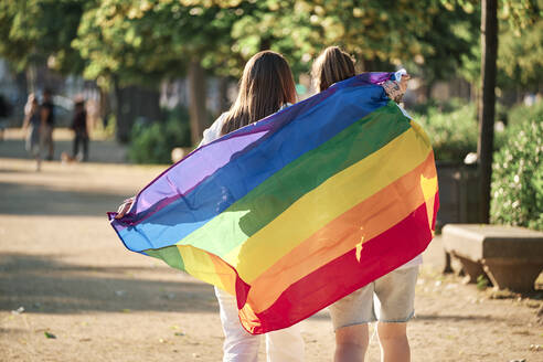 Lesbian couple holding rainbow flag while walking at park - AGOF00153
