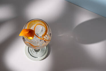 Draufsicht auf ein transparentes Glas mit einem Highball-Cocktail, dekoriert mit Zitrusfruchtschalen und Nelken im Schatten des Sonnenlichts - ADSF25202