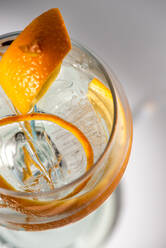Draufsicht auf ein transparentes Glas mit einem Highball-Cocktail, dekoriert mit Zitrusfruchtschalen und Nelken im Schatten des Sonnenlichts - ADSF25204