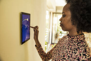Afro woman using home automation device on wall - UUF23535