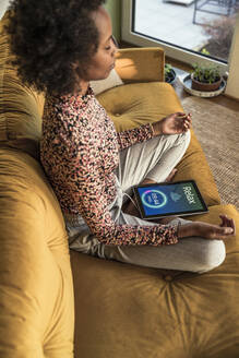 Frau meditiert im Sitzen mit Timer auf digitalem Tablet zu Hause - UUF23553