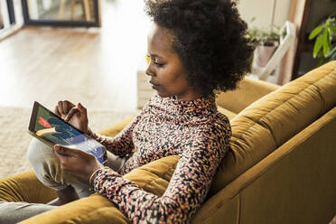 Woman examining pulse trace on digital tablet while sitting on sofa - UUF23555