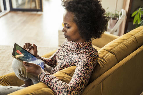 Frau, die auf dem Sofa sitzend die Pulsspur auf einem digitalen Tablet untersucht - UUF23555