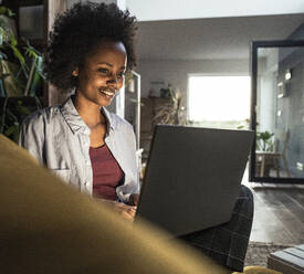 Smiling businesswoman using laptop while sitting at home - UUF23567