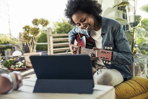 Junge Frau übt Gitarre beim E-Learning über ein digitales Tablet zu Hause - UUF23581