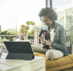 Frau übt zu Hause durch E-Learning auf einem digitalen Tablet Gitarre - UUF23582