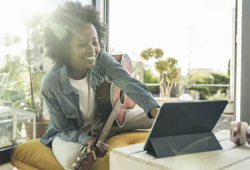 Woman with guitar using digital tablet while sitting at home - UUF23583