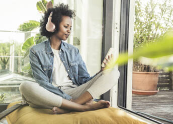 Woman with headphones using mobile phone while sitting on cushion - UUF23587