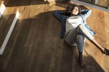 Young woman relaxing on hardwood floor at home - UUF23593