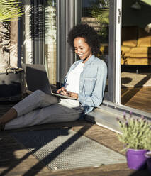 Young woman using laptop while sitting at balcony - UUF23595