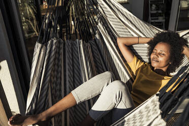 Smiling woman with hands behind head relaxing on hammock during sunny day - UUF23597