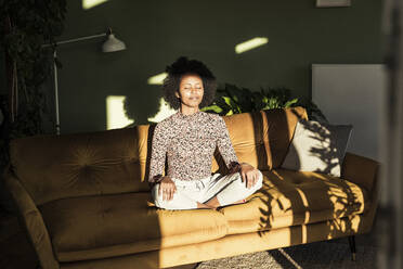 Junge Frau übt Yoga im Schneidersitz auf dem Sofa - UUF23607