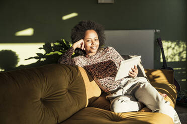 Frau hält digitales Tablet, während sie im Wohnzimmer sitzt - UUF23620