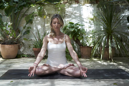 Mature woman meditating in lotus positing on exercise mat - VEGF04676