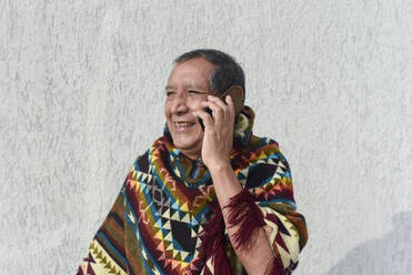Lächelnder älterer Mann, der vor einer grauen Wand mit einem Mobiltelefon spricht - DSIF00442