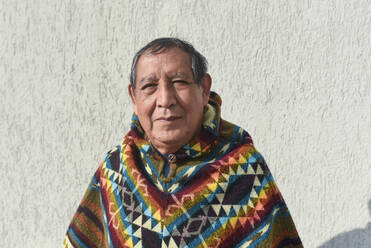 Älterer indigener Mann mit Poncho vor einer Mauer - DSIF00444