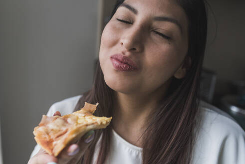 Woman with eyes closed eating pizza at home - DSIF00455