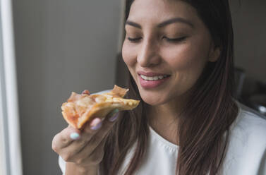 Lächelnde Frau hält Pizzastück zu Hause - DSIF00456