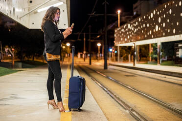 Berufstätige Frau benutzt Mobiltelefon auf dem Bahnsteig der Straßenbahn - DLTSF01914