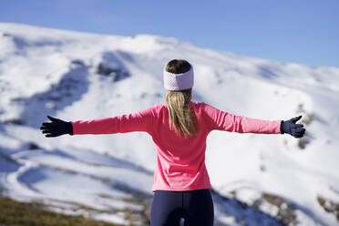 Weibliche Athletin mit ausgestreckten Armen vor einem schneebedeckten Berg stehend - JSMF02374