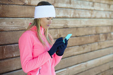 Frau benutzt Smartphone vor einer Holzwand - JSMF02388