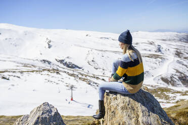 Junge Frau mit Strickmütze sitzt auf einem Felsen und genießt ihren Urlaub - JSMF02397