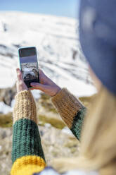 Frau fotografiert im Winter schneebedeckten Berg mit dem Handy - JSMF02400