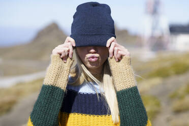 Young woman puckering while covering eyes with knit hat - JSMF02403