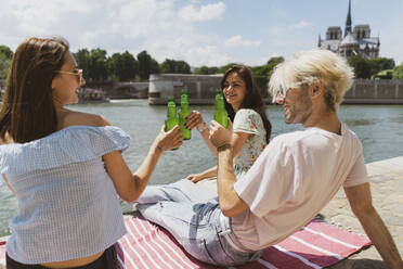 Man smiling while raising toasts with female friends during sunny day - AFVF08944