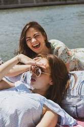 Woman laughing while female friend looking away during sunny day - AFVF08949