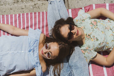 Female friends lying on leg of man during summer - AFVF08950