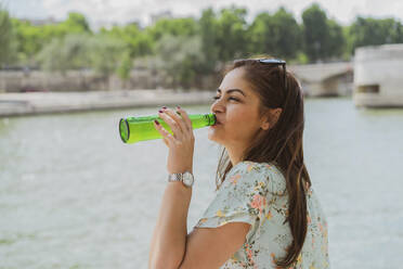 Young woman drinking beer by river during vacations - AFVF08955