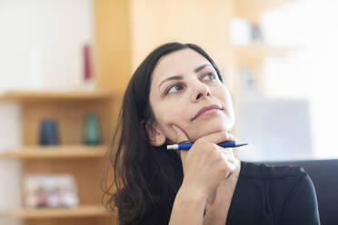 Thoughtful female professional with hand on chin looking away while sitting in office - SGF02833