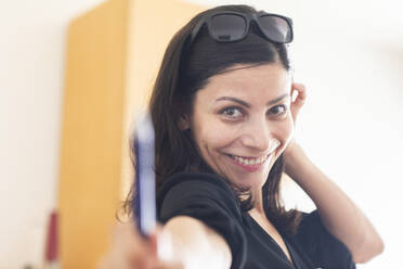 Glückliche Geschäftsfrau mit Sonnenbrille, die im Büro stehend einen Stift gibt - SGF02834