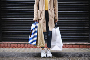 Woman holding shopping bags in front of closed shutter - ASGF00617