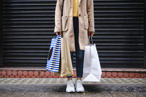 Frau mit Einkaufstüten vor geschlossenem Rollladen - ASGF00617