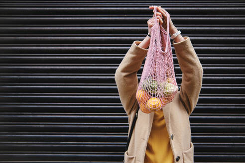 Woman holding mesh bag near shutter - ASGF00623