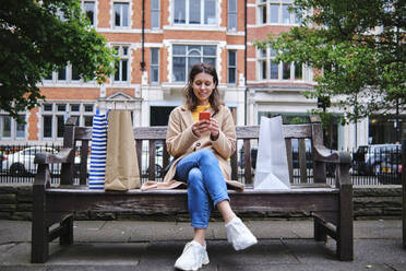 Frau sitzt auf einer Bank und benutzt ein Smartphone in der Stadt - ASGF00625