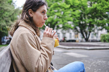 Contemplating woman drinking smoothie while sitting on bench - ASGF00630