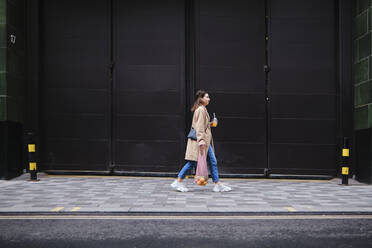 Junge Frau geht auf dem Fußweg durch schwarze Türen - ASGF00632