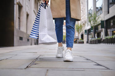 Woman with shopping bags walking on footpath - ASGF00637