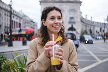 Thoughtful woman holding juice glass in city - ASGF00639