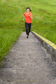 Junge Frau joggt auf Stufen inmitten von Gras auf einem Hügel - STSF02975