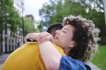 Happy young woman with eyes closed hugging boyfriend at park - ASGF00642