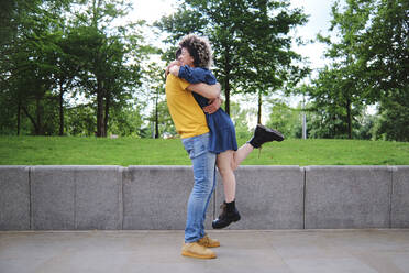 Young man lifting girlfriend while hugging at park - ASGF00643