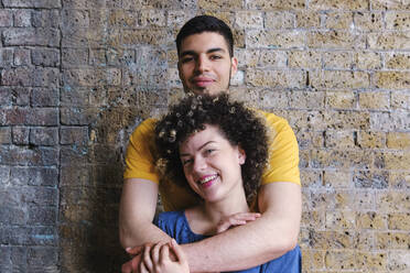 Happy curly haired woman standing with boyfriend in front of wall - ASGF00660