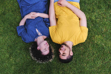 Lächelndes junges Paar, das zusammen auf dem Rasen eines Parks liegt - ASGF00665