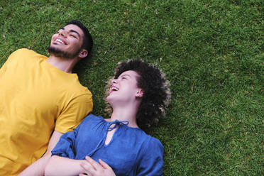 Happy young couple lying together on grass at park - ASGF00666