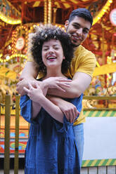 Fröhliches junges Paar, das sich in einem Vergnügungspark in den Armen liegt - ASGF00672