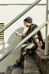Junger Mann, der auf einer Treppe sitzend mit seinem Smartphone im Internet surft - AFVF08969